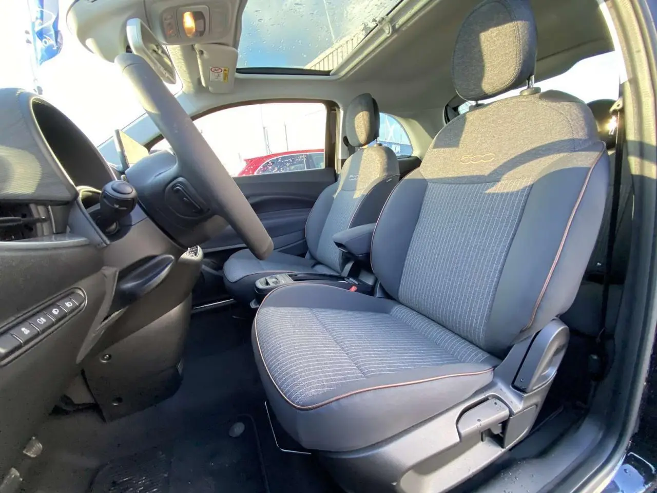 Intérieur côté conducteur d'une FIAT 500 électrique noire 2022, sièges gris avec logo 500 et toit panoramique visible.