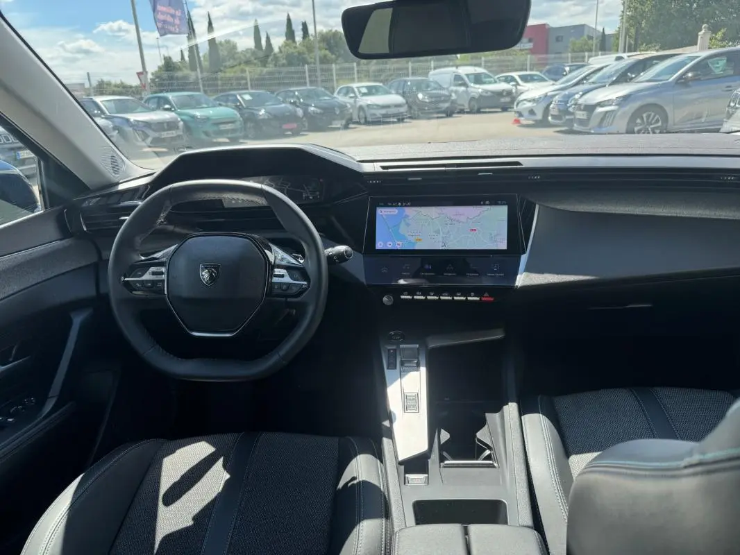 Intérieur noir de la Peugeot 308 Hybrid 2024 vu de face, avec volant compact et écran tactile central affichant une carte.