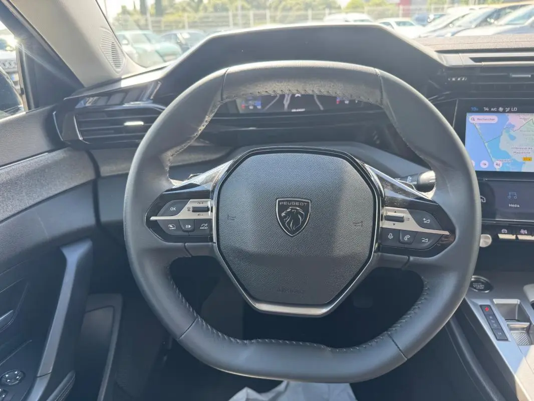 Vue centrée sur le volant noir du Peugeot 308 Hybrid 2024, avec tableau de bord numérique et écran tactile visible.