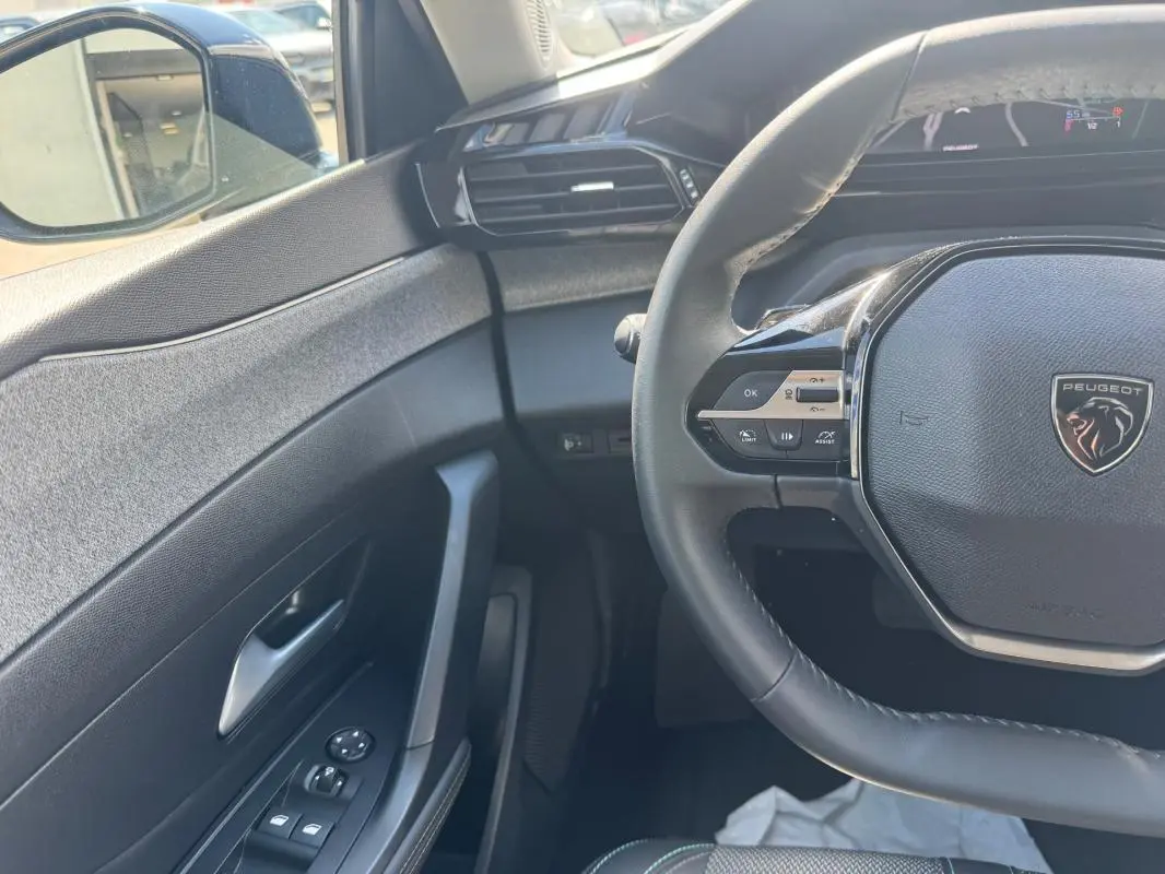 Vue intérieure côté conducteur de la Peugeot 308 Hybrid 2024 noire, volant multifonction et commandes sur porte visibles.