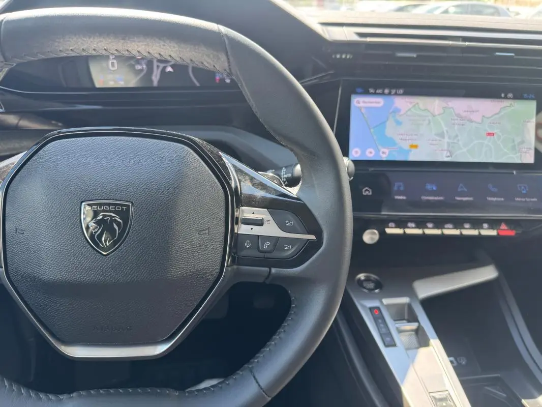 Vue intérieure centrée sur le volant Peugeot noir et le cockpit numérique avec écran tactile affichant une carte.