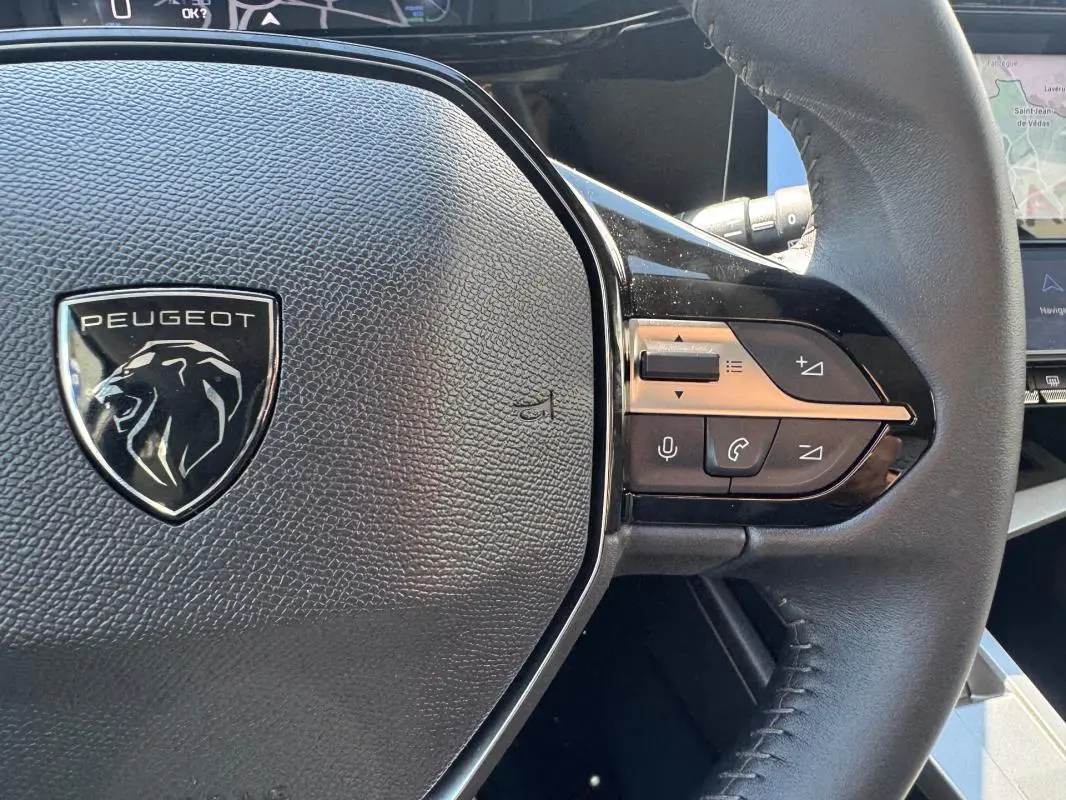Gros plan sur le volant noir de la Peugeot 308 Hybrid 136 e-DCS6 Allure avec commandes intégrées à droite.