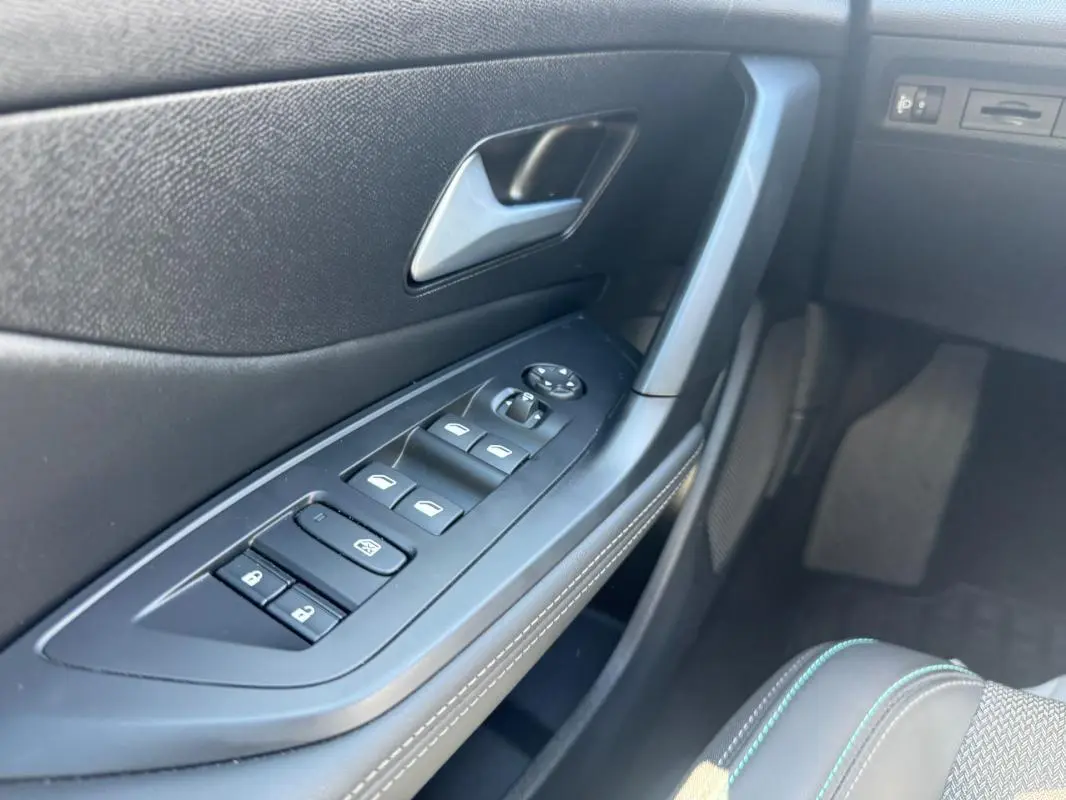 Gros plan sur la porte côté conducteur de la Peugeot 308 Hybrid noire, montrant les commandes des vitres et la poignée intérieure.
