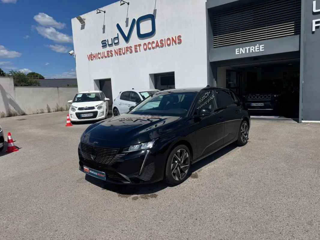 PEUGEOT 308 Hybrid noir vue 3/4 avant droit, jantes alliage 17 pouces, stationnée devant un garage Sud VO.