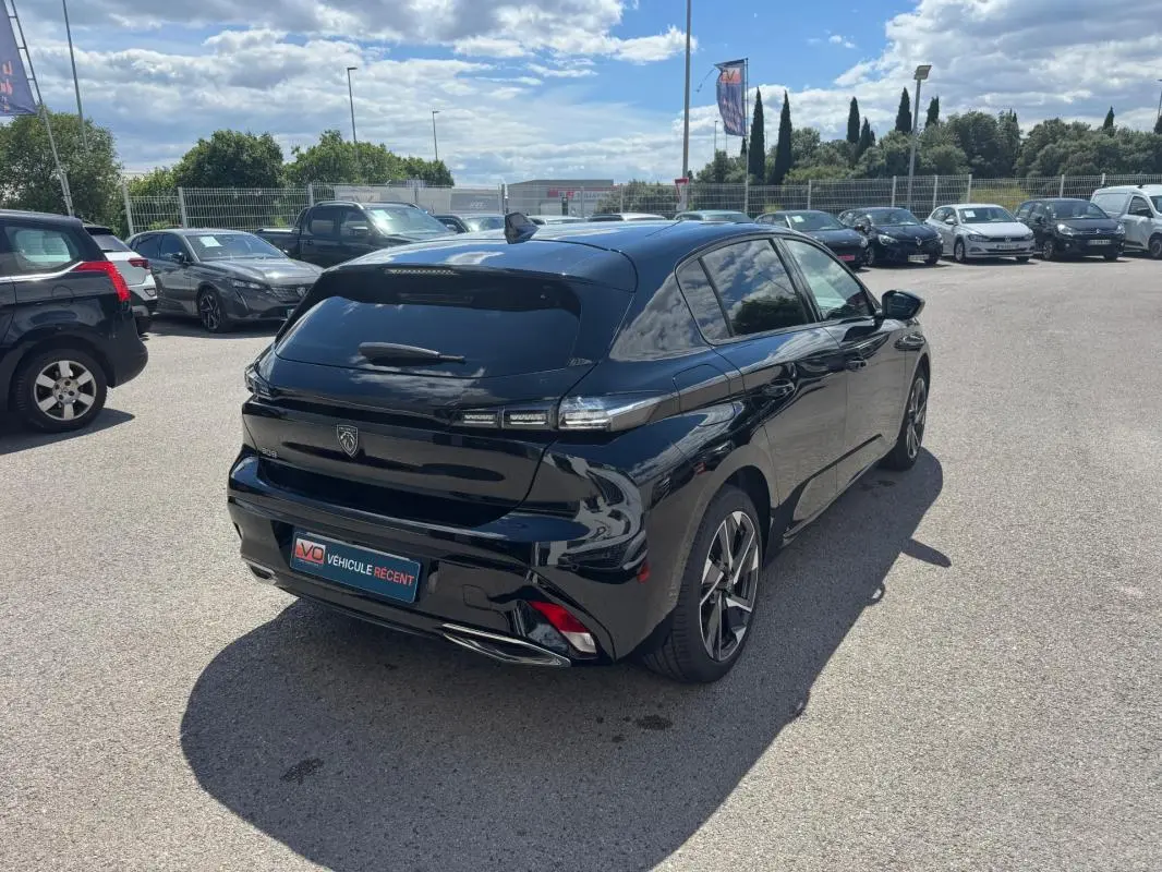 Vue 3/4 arrière droite d'une Peugeot 308 Hybrid 136 noire avec jantes alliage 17 pouces, stationnée en extérieur.