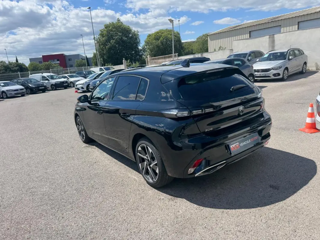 Vue 3/4 arrière droite d'une Peugeot 308 Hybrid noire 2024 avec jantes alliage 17 pouces, feux LED et toit noir brillant.