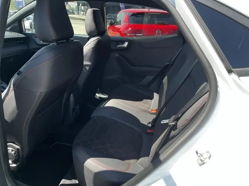 Vue intérieure arrière côté droit du Ford Puma blanc 2025, sièges en tissu noir avec surpiqûres rouges visibles.