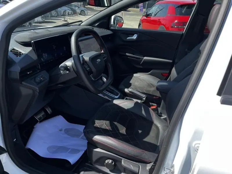 Vue intérieure côté conducteur du Ford Puma blanc 2025, mettant en valeur le tableau de bord numérique et les sièges en cuir avec surpiqûres rouges.