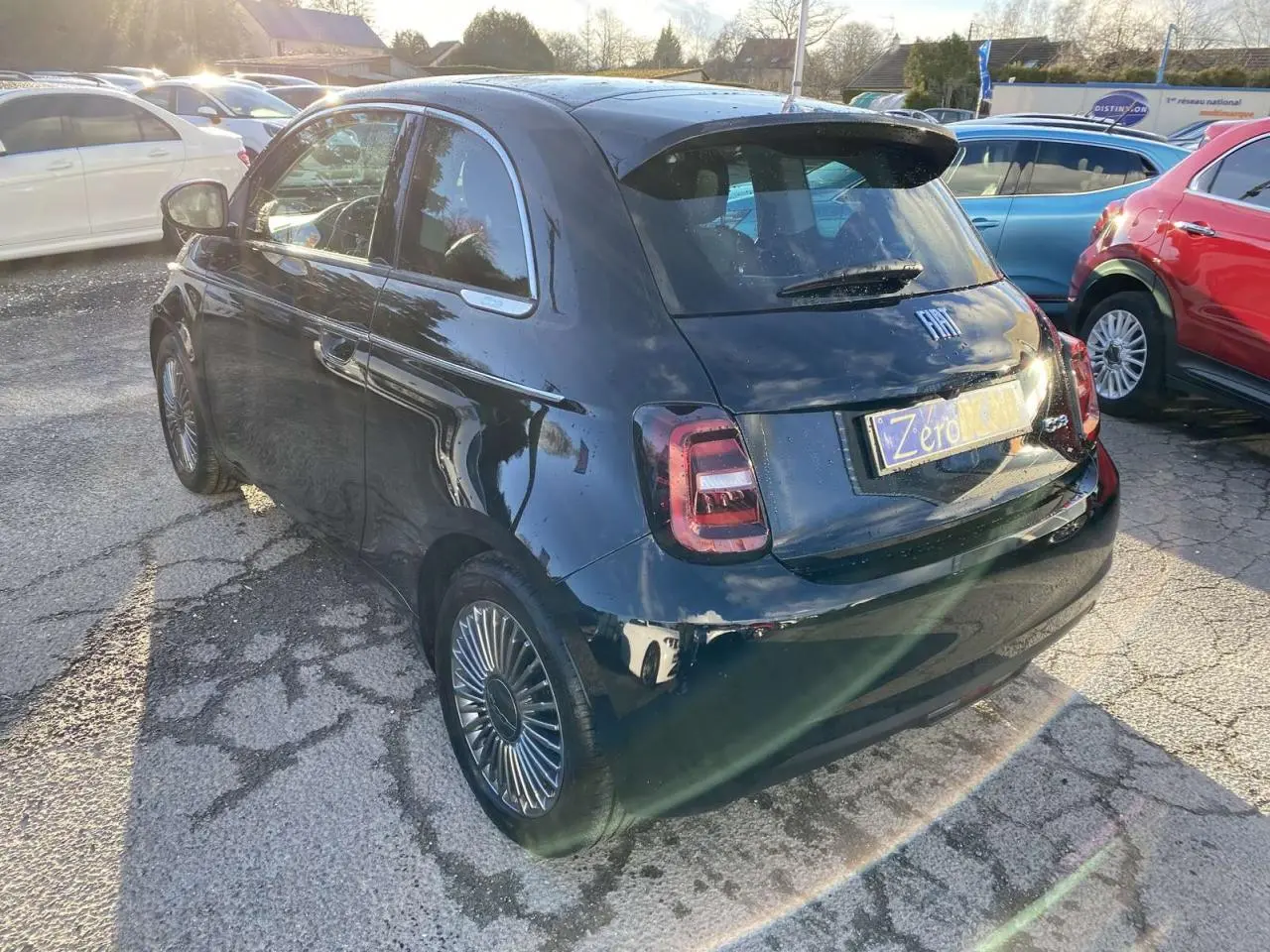 Vue 3/4 arrière droite d'une Fiat 500 électrique noire 2022 avec jantes stylisées et toit vitré panoramique