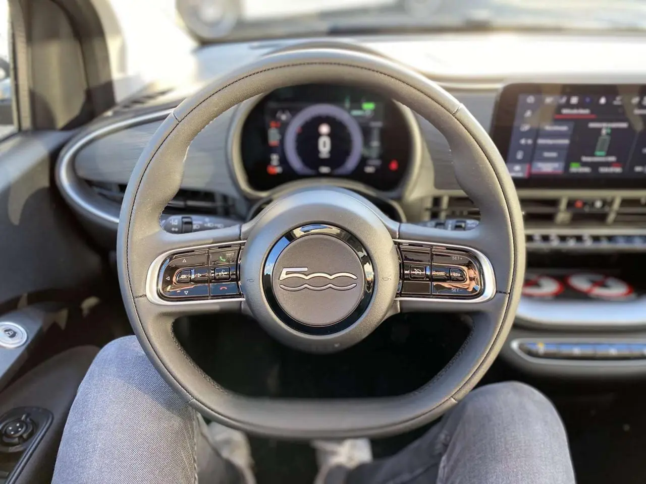 Vue intérieure centrée sur le volant noir de la Fiat 500 électrique 2022 avec tableau de bord numérique et écran tactile.