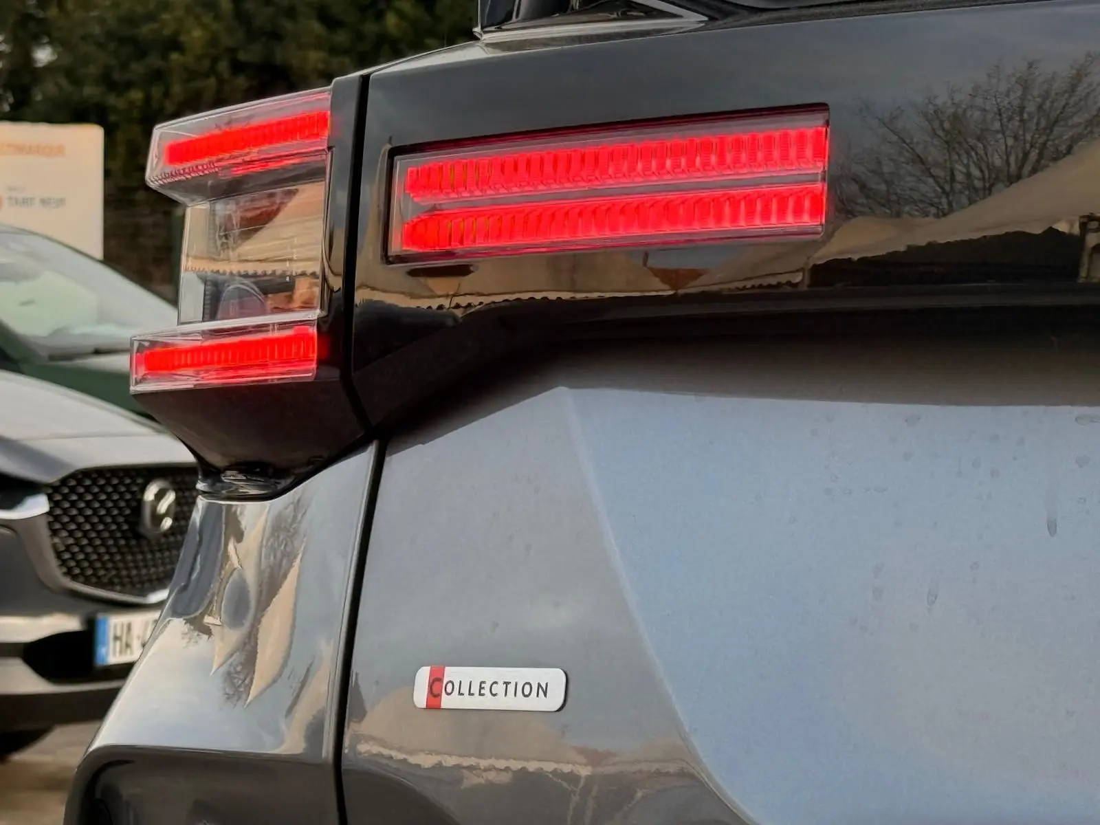 Gros plan sur le feu arrière droit rouge vif et l’insigne Collection d’une Citroën C4 hybride gris Mercury.