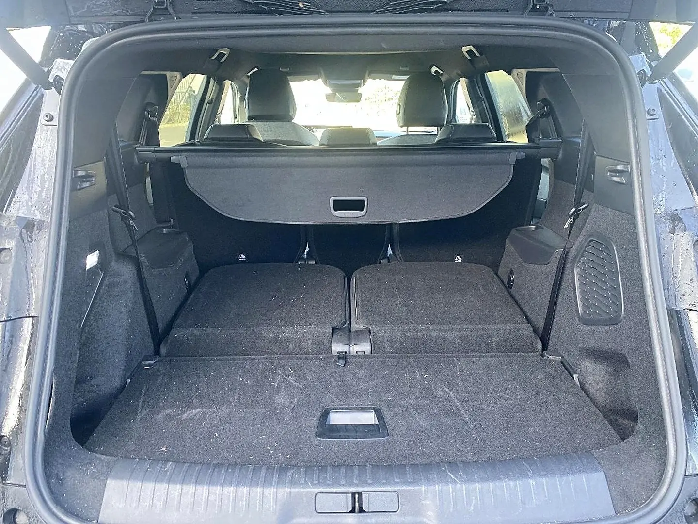 Coffre ouvert du Peugeot 5008 noir, vue arrière montrant banquette rabattue et cache-bagages en place.