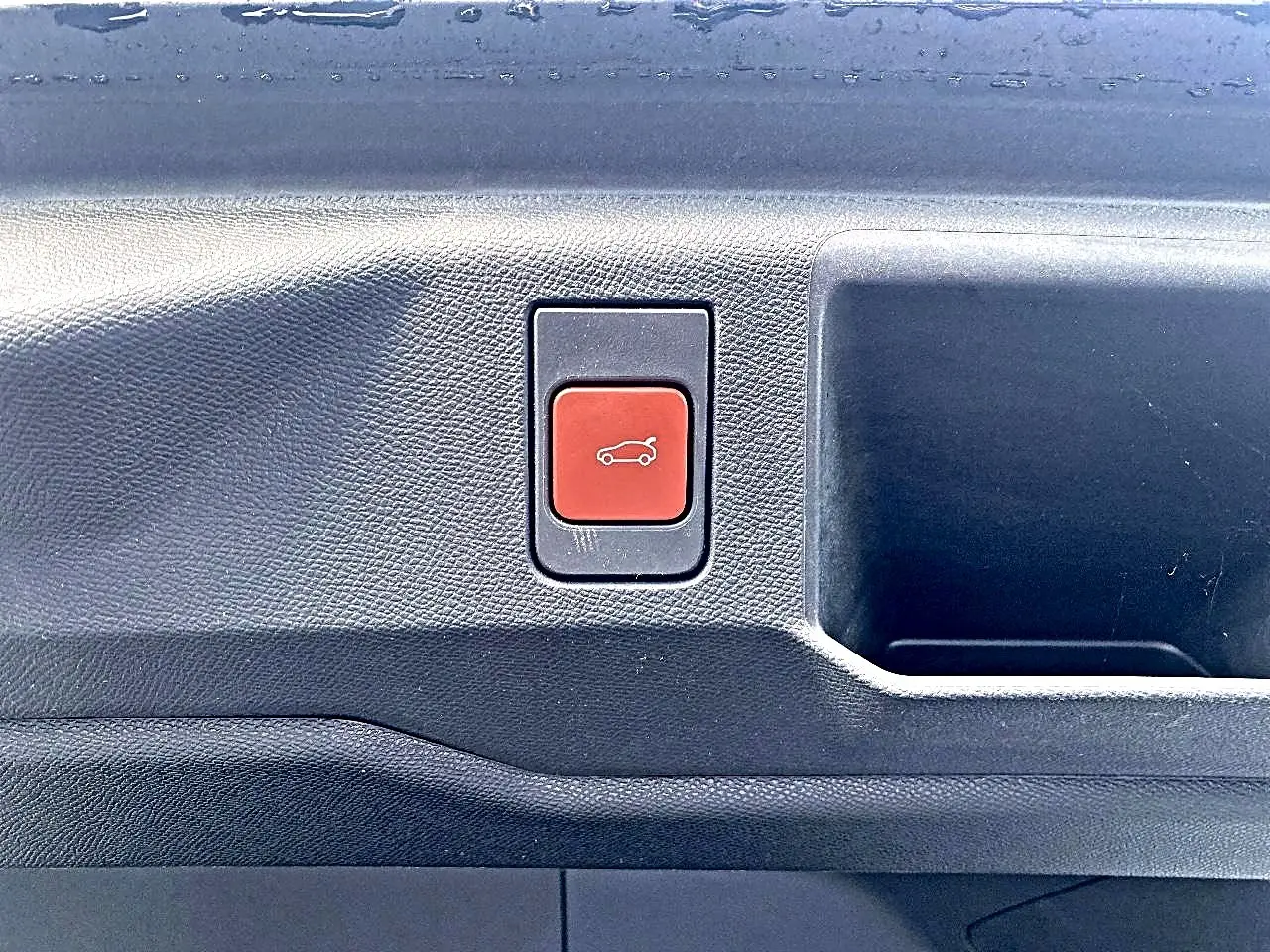 Bouton rouge d'ouverture électrique du coffre sur la garniture intérieure noire d'un Peugeot 5008 Hybrid 145 GT e-dcs6.
