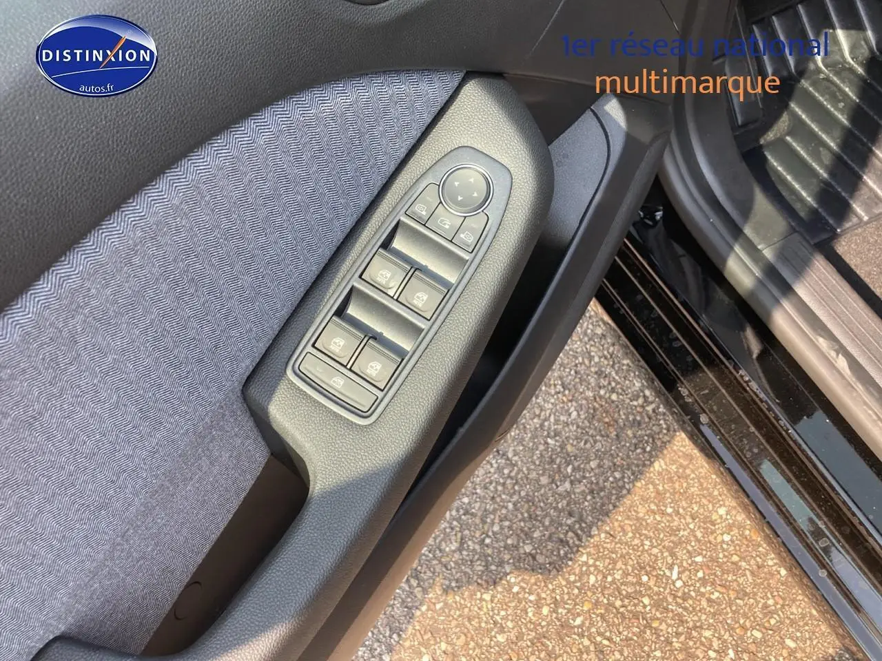 Gros plan sur la commande des vitres côté conducteur de la Renault Clio V noire Étoile, avec tissu gris et plastique noir.