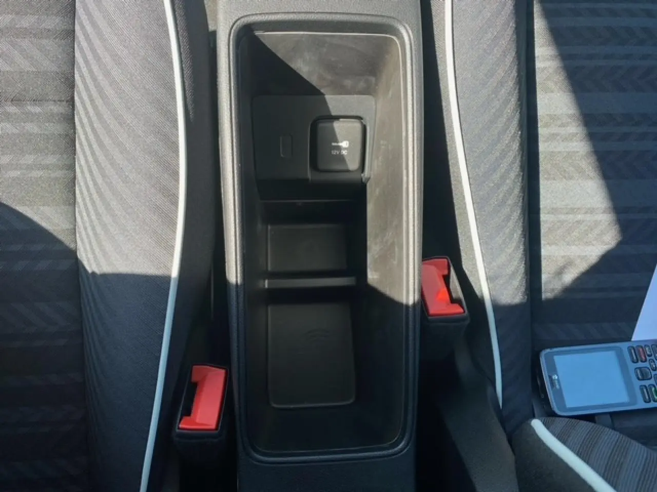 Vue plongeante sur la console centrale noire de la Fiat 500 électrique blanche avec sièges gris et ceintures rouges.