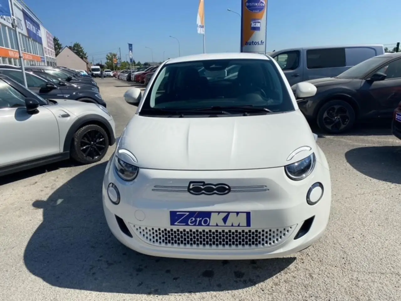 Vue frontale d'une FIAT 500 électrique blanche Ice White avec logo 500 et plaque Zéro KM visible.