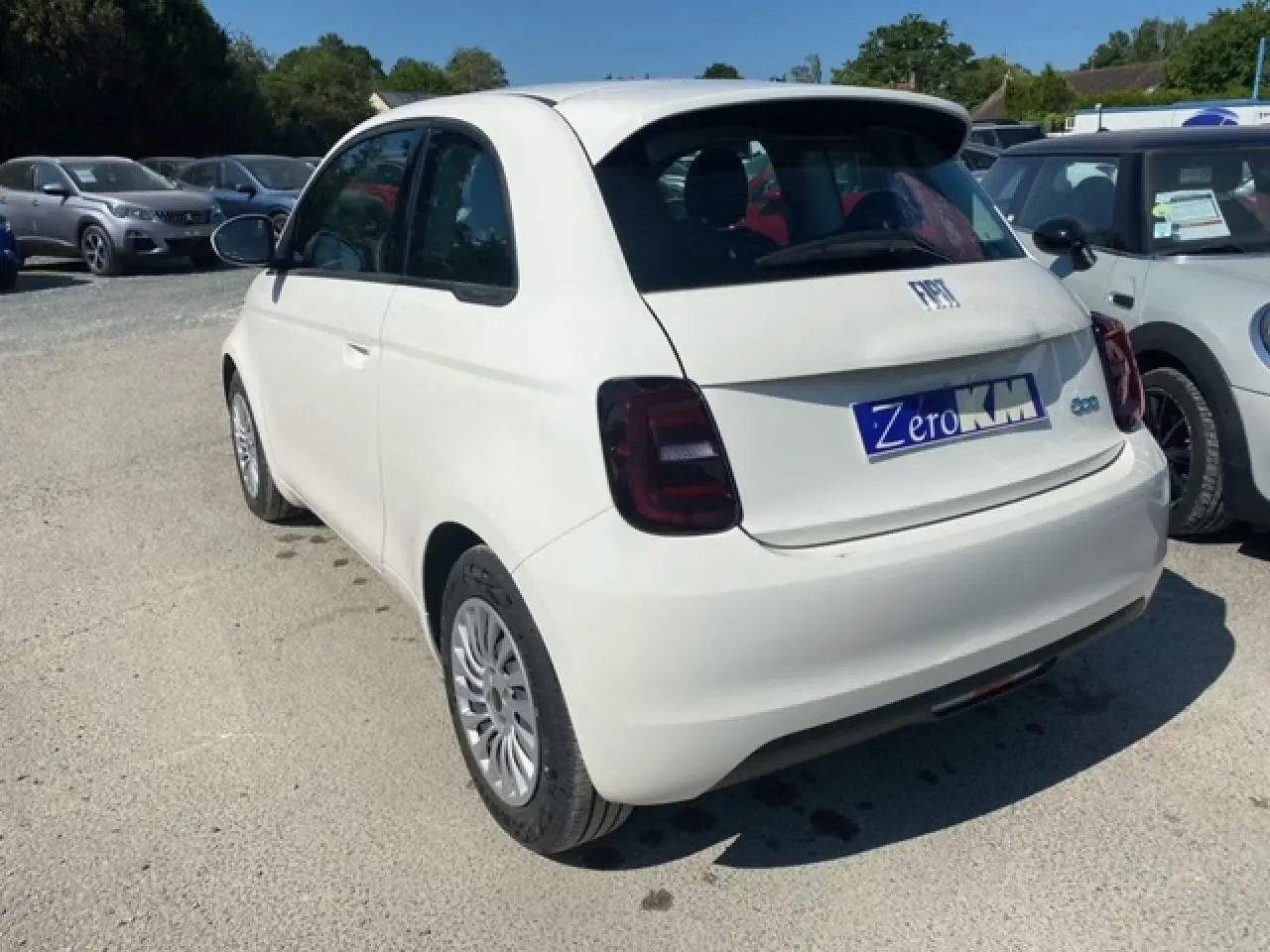 Vue 3/4 arrière droite d'une FIAT 500 électrique blanche Ice White avec feux arrière foncés sur parking extérieur.