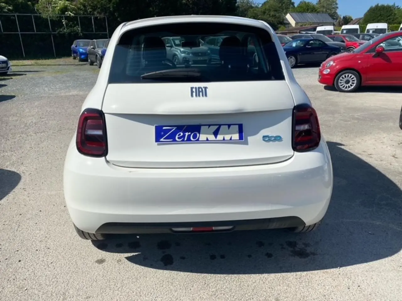 Vue arrière d'une FIAT 500 électrique blanche avec feux arrière foncés et plaque "Zero KM" visible.