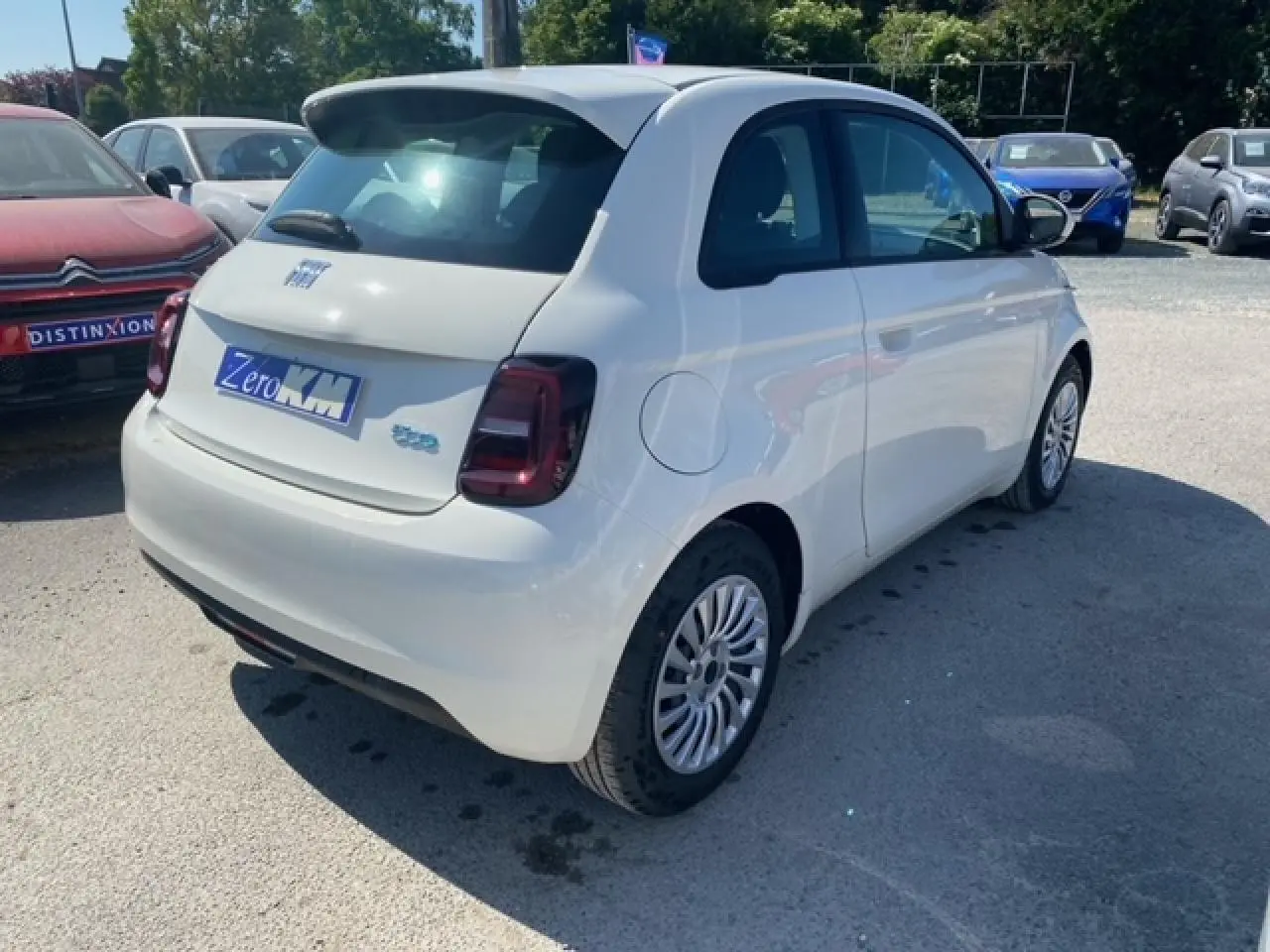 Vue 3/4 arrière droite d'une FIAT 500 électrique blanche Ice White avec feux arrière foncés sur parking extérieur.