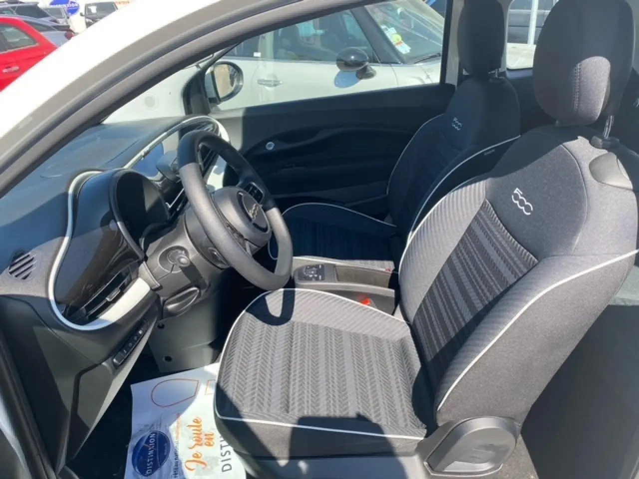 Intérieur avant droit de la Fiat 500 électrique blanche 2022, sièges noirs avec logo 500 brodé et tableau de bord moderne.