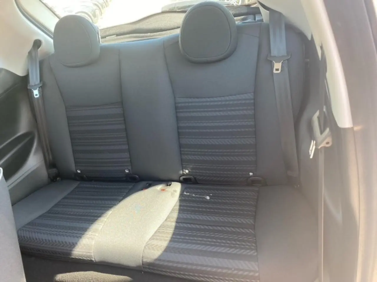 Vue intérieure arrière des sièges noirs de la Fiat 500 électrique blanche, montrant les appuie-têtes et ceintures de sécurité.