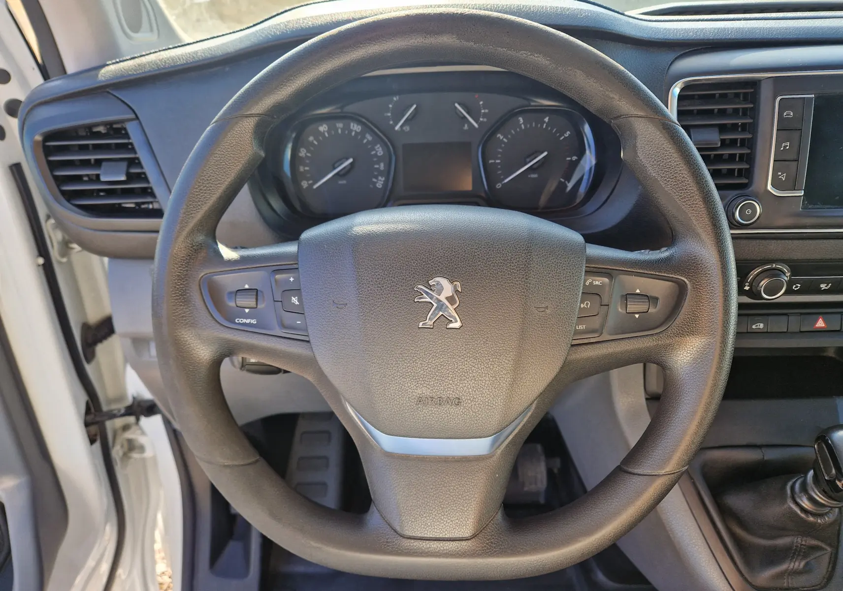 Vue rapprochée du volant noir du Peugeot Expert Fourgon blanc 2020, avec tableau de bord et levier de vitesses manuelle visibles.