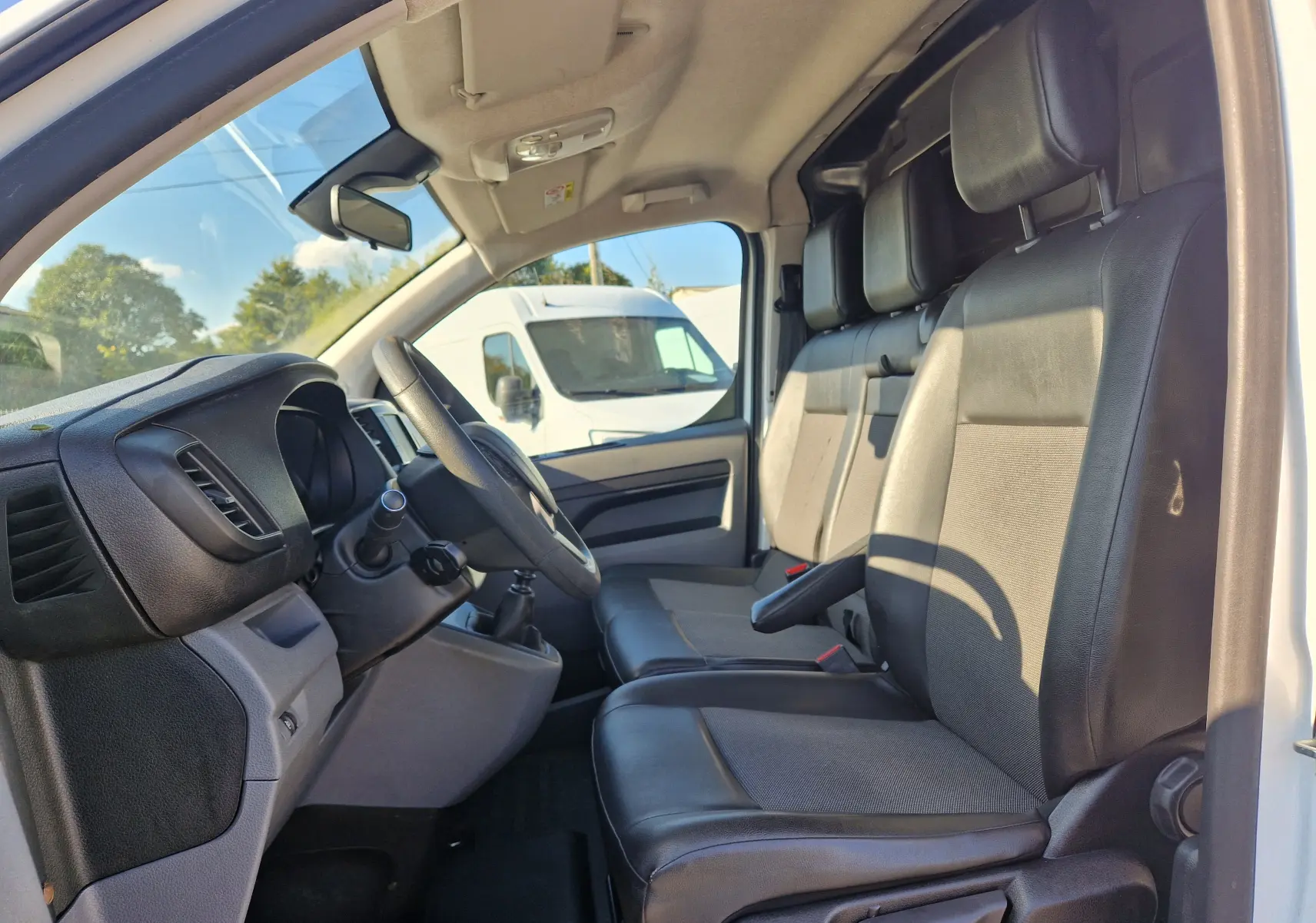 Vue intérieure côté conducteur du Peugeot Expert Fourgon blanc 2020, montrant les sièges en cuir et le tableau de bord.