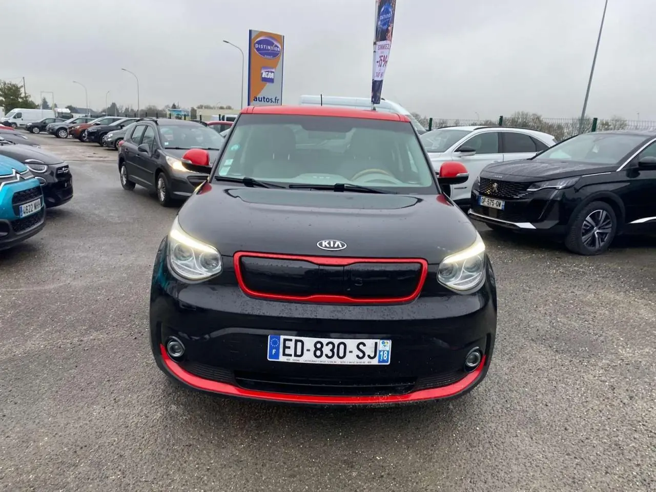 Vue avant d'une KIA Soul électrique noire avec toit et détails rouges, feux allumés sur parking extérieur.