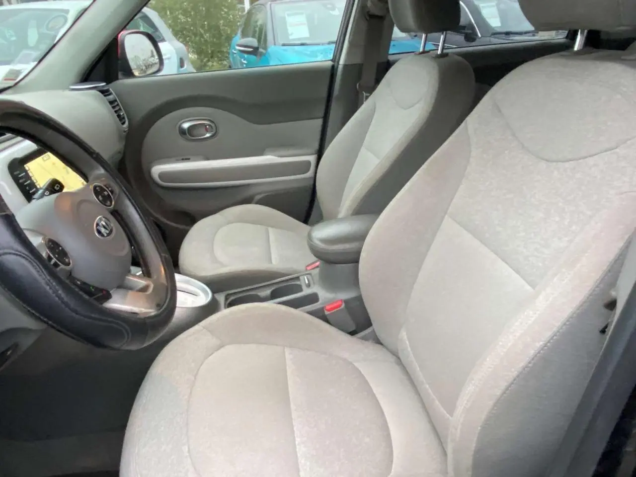 Intérieur avant du Kia Soul électrique 2016, sièges gris clairs et tableau de bord avec écran tactile visible.