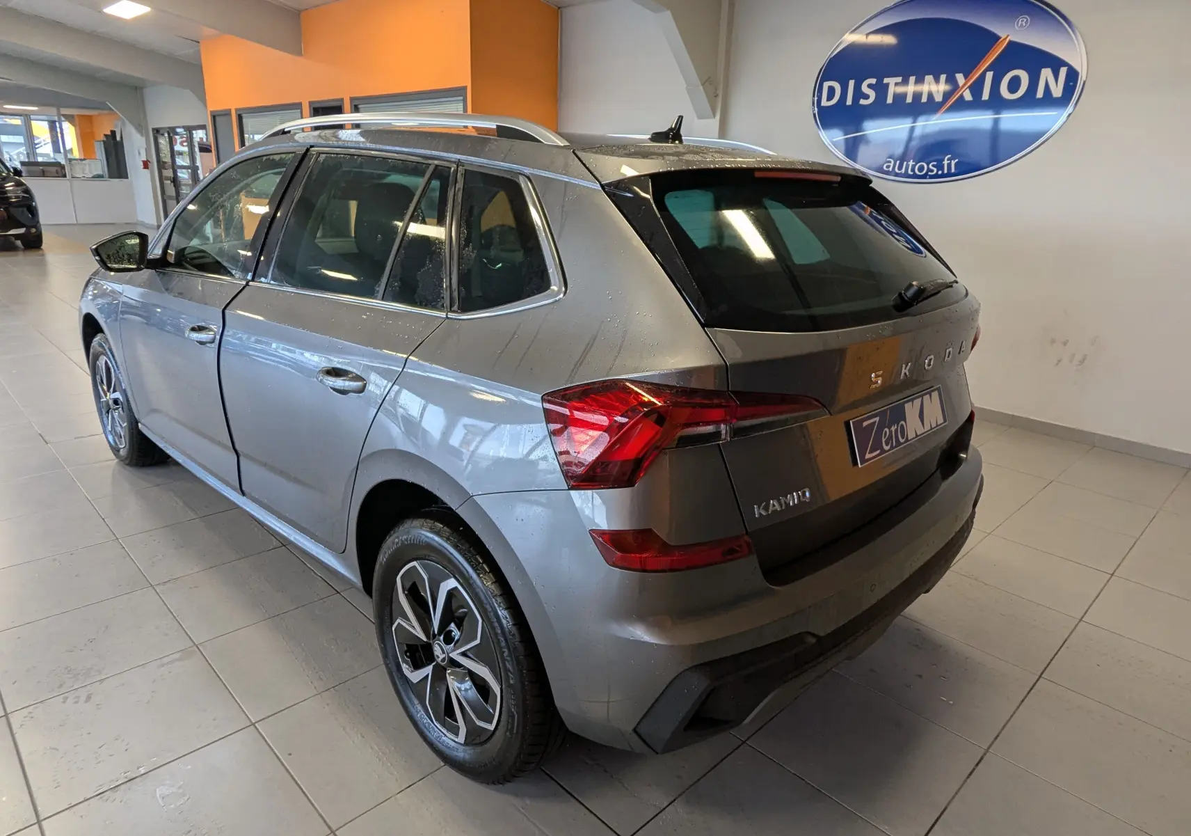Vue 3/4 arrière droite d’un Skoda Kamiq gris graphite métal 2025 avec jantes alliage et feux LED, en intérieur showroom.