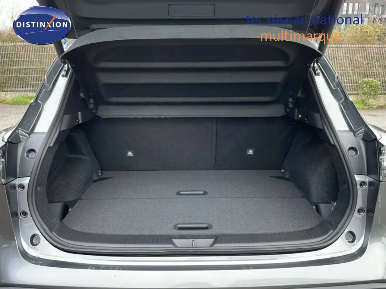Coffre ouvert vu de l'arrière du Nissan Qashqai 1.5 E-POWER gris squale métal, montrant un espace de chargement plat et spacieux.