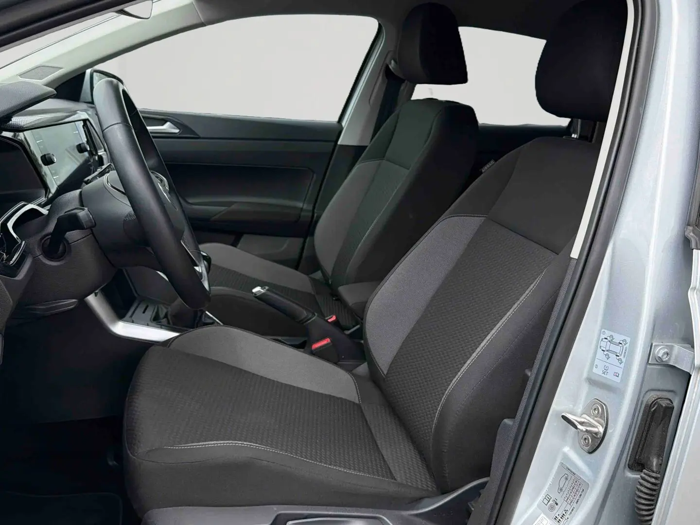 Vue intérieure côté conducteur de la Volkswagen Polo 2025 gris, montrant sièges tissu noirs et tableau de bord moderne.