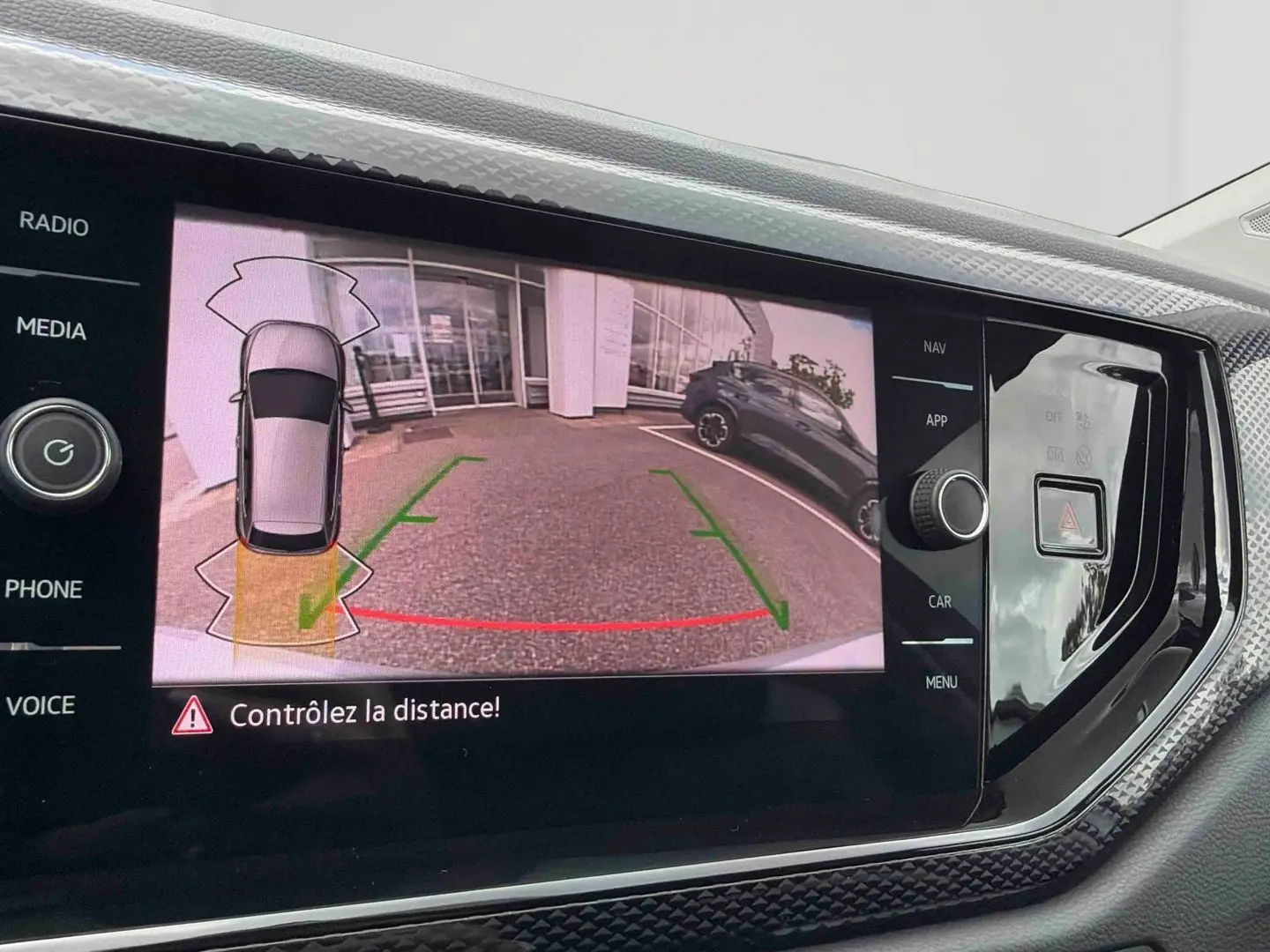 Écran de caméra de recul affichant l’arrière d’une Volkswagen Polo grise en stationnement, vue intérieure console centrale.