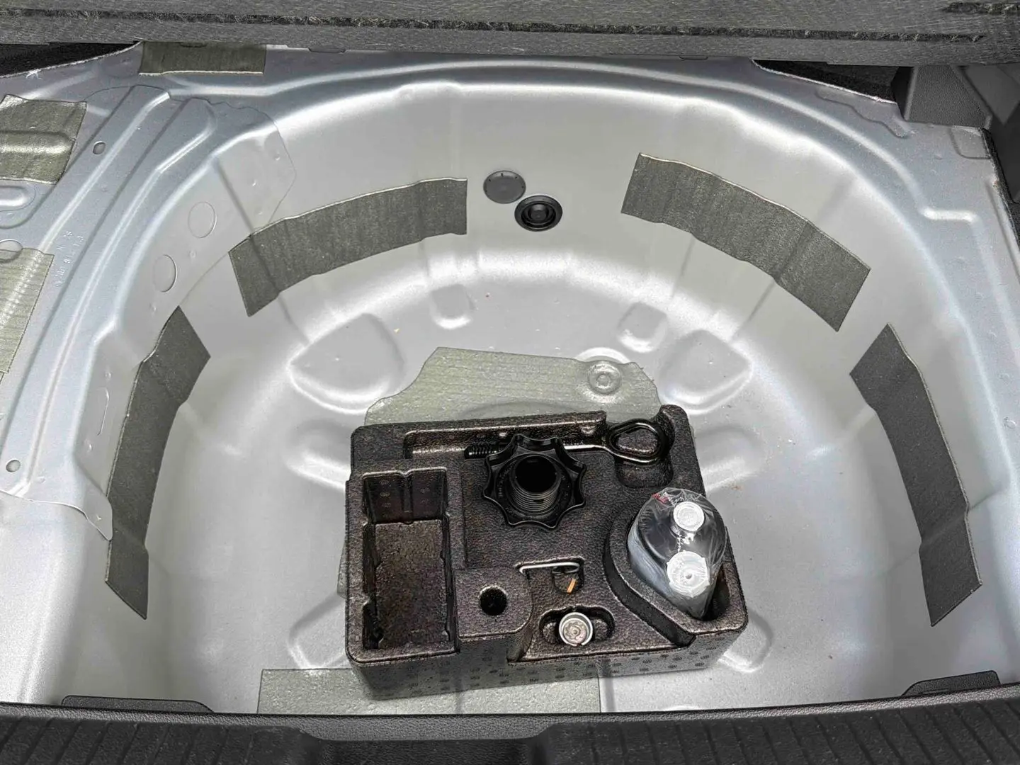 Vue plongeante sur le coffre ouvert d'une Volkswagen Polo grise, montrant le rangement pour roue de secours et outils.