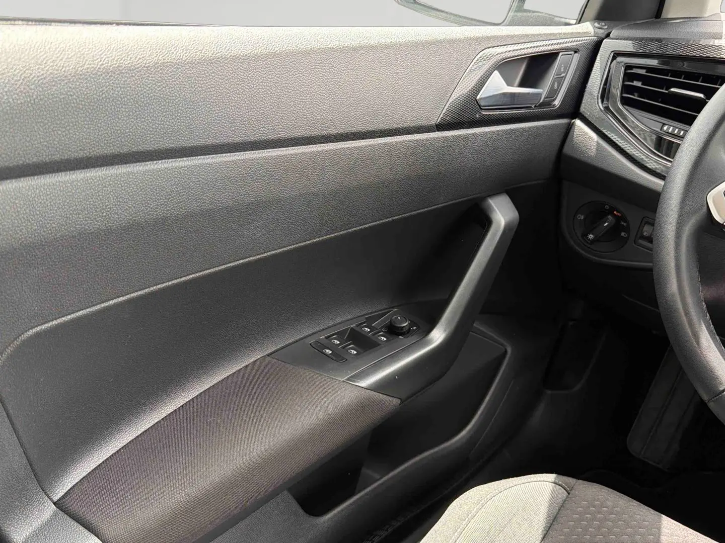 Vue intérieure côté conducteur de la Volkswagen Polo 2025, montrant la portière avec commandes électriques et accoudoir gris foncé.