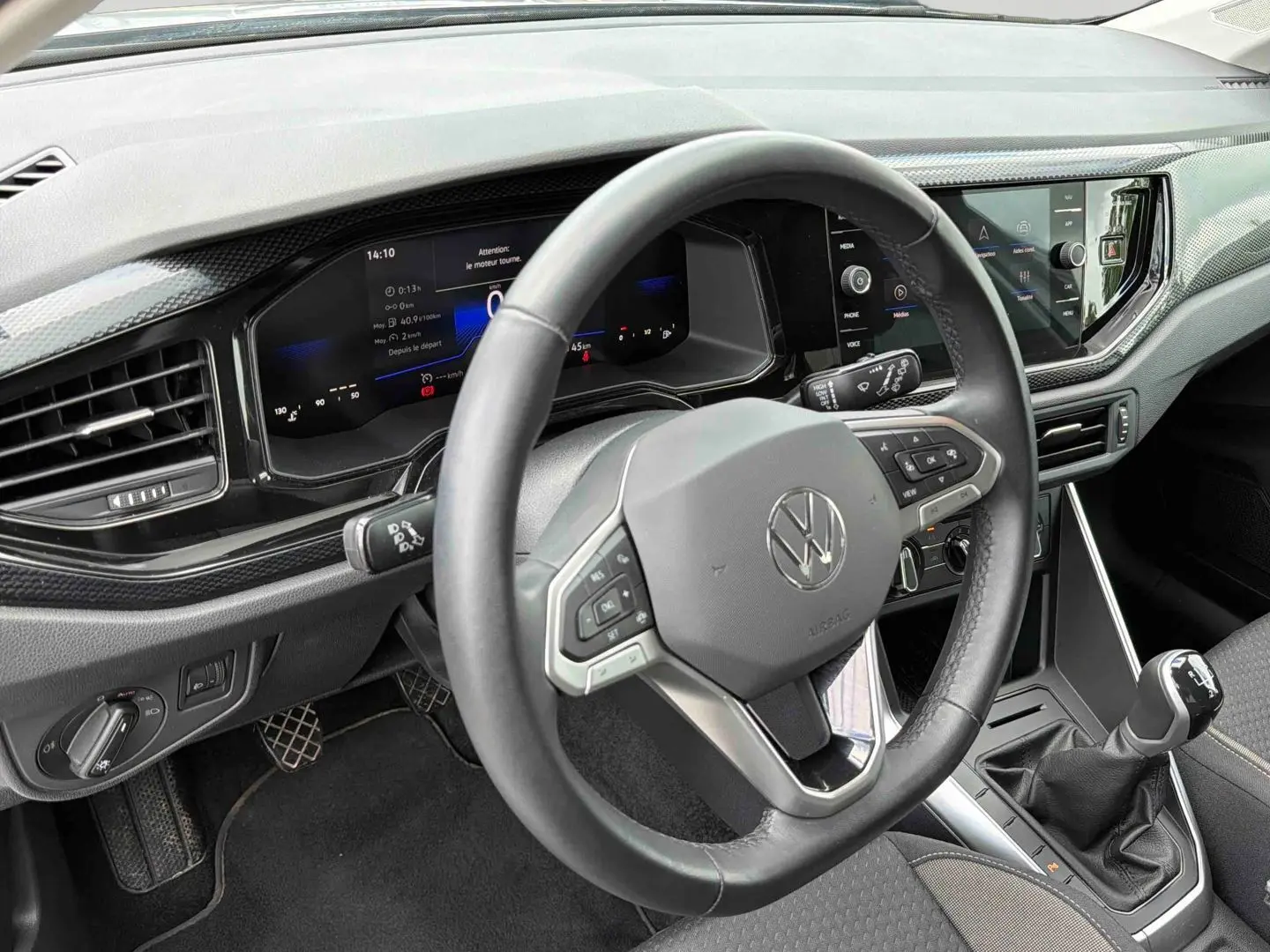 Vue intérieure côté conducteur du tableau de bord gris et volant multifonctions d'une Volkswagen Polo 2025 avec boîte manuelle.