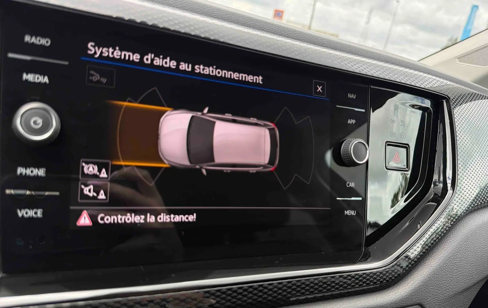 Écran tactile central du Volkswagen Polo 2025 montrant l'aide au stationnement avec vue aérienne du véhicule gris.