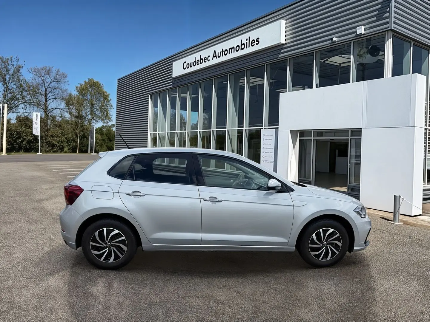 Profil côté droit de la Volkswagen Polo grise 2025 avec jantes alliage, stationnée devant un showroom moderne.