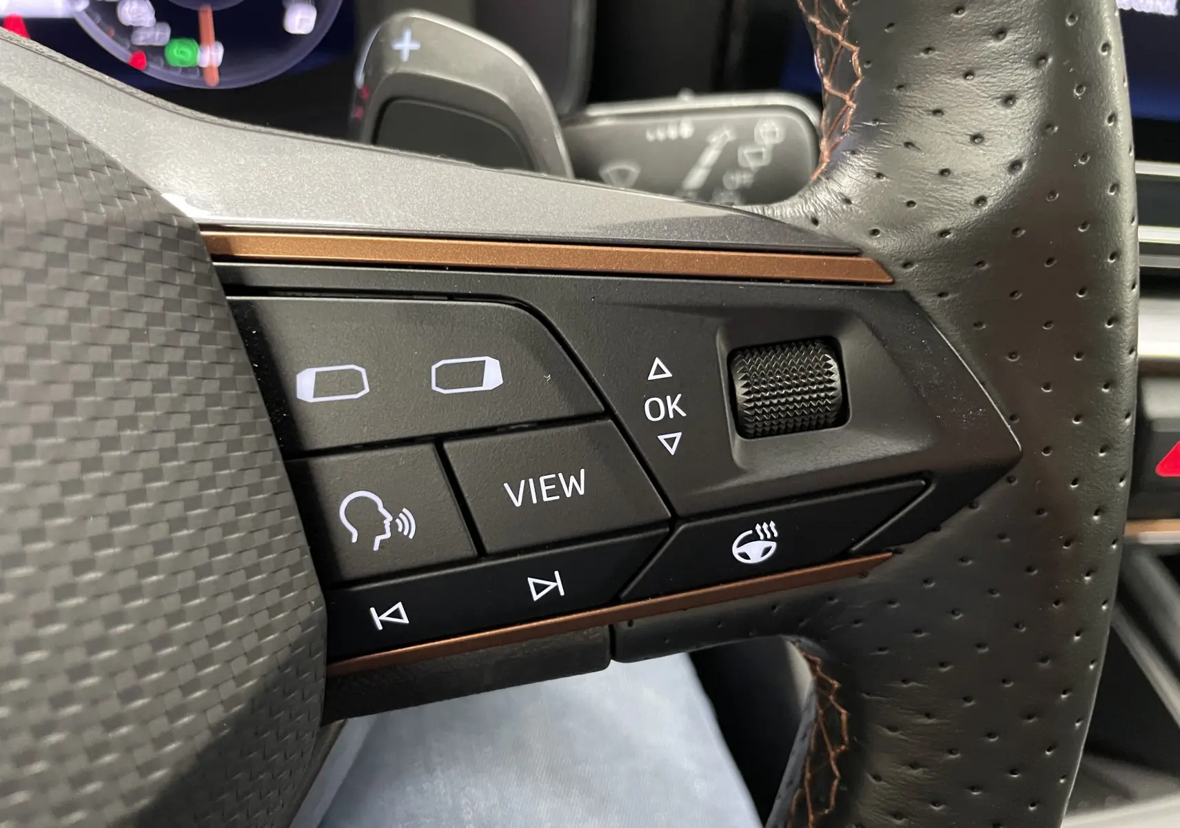 Gros plan sur les commandes gauche du volant perforé du CUPRA Formentor 2023 avec surpiqûres cuivrées et boutons fonctionnels.