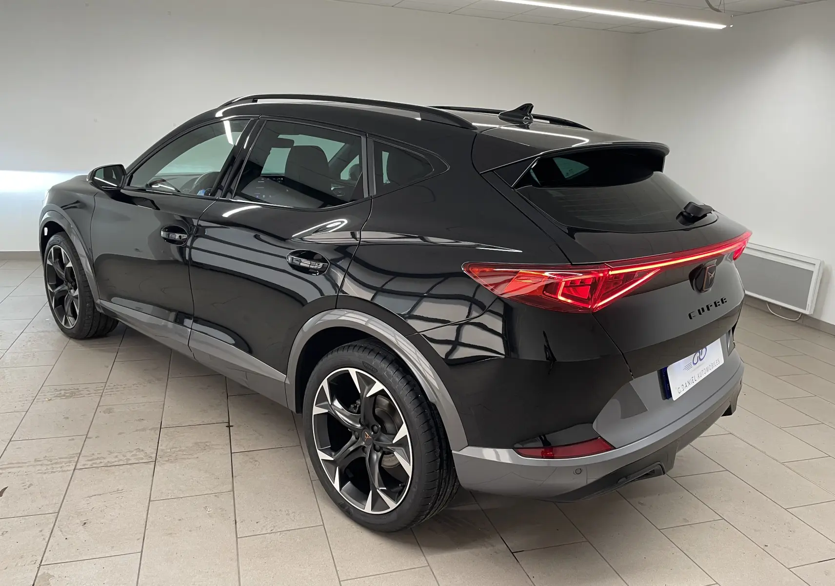 Vue 3/4 arrière côté gauche d'un CUPRA Formentor Noir Minuit avec feux arrière allumés et jantes noires sport