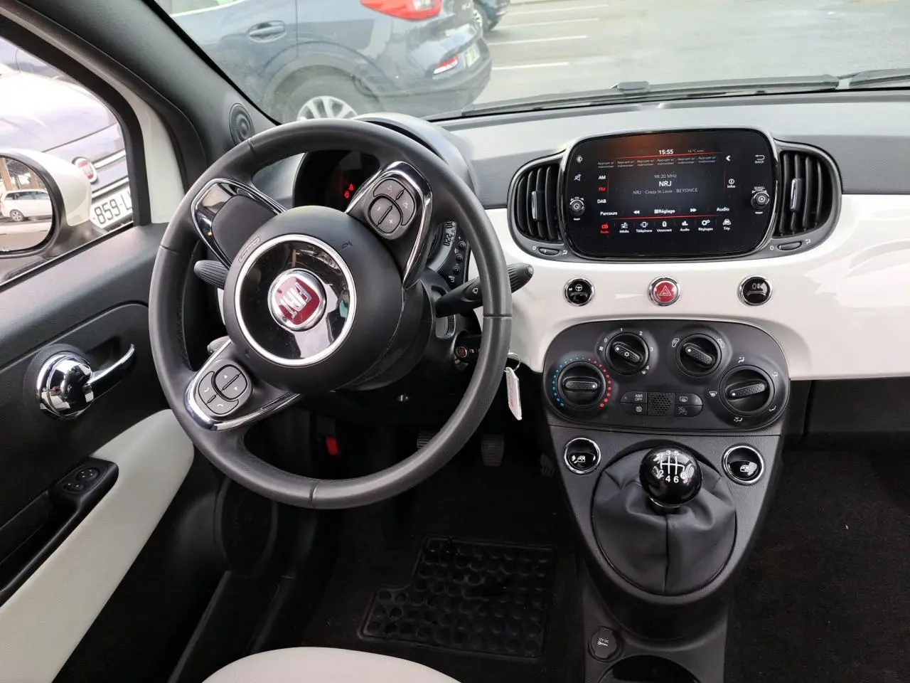 Intérieur de Fiat 500 Cabriolet blanc 2021, vue du poste de conduite avec volant, tableau de bord et levier de vitesses manuel.