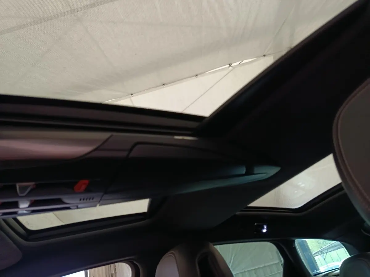 Toit panoramique ouvert vu de l'intérieur arrière d'une DS5 noire, avec sièges en cuir visibles.