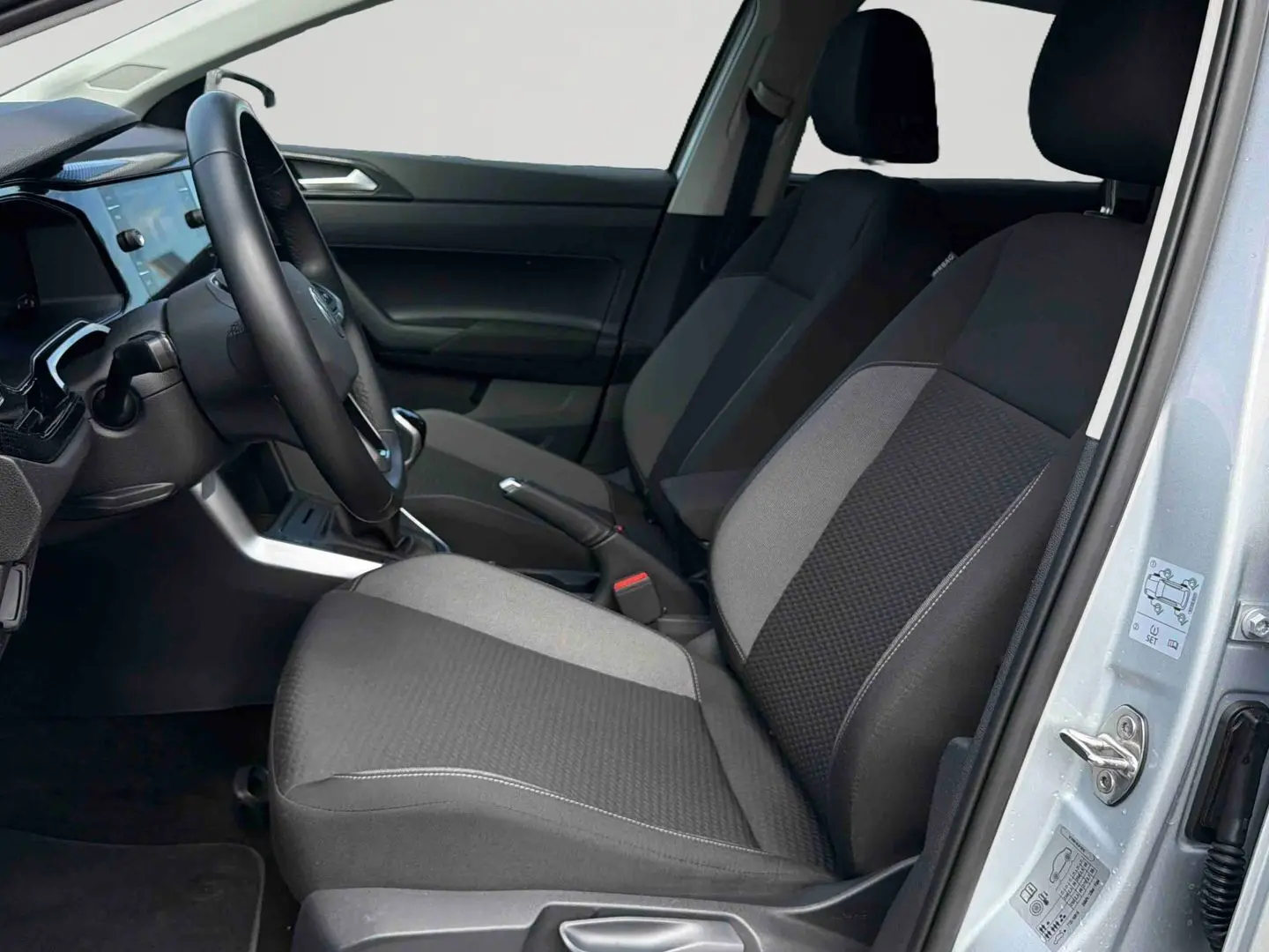 Vue intérieure côté conducteur de la Volkswagen Polo grise 2025, sièges tissu bicolore et volant multifonctions.