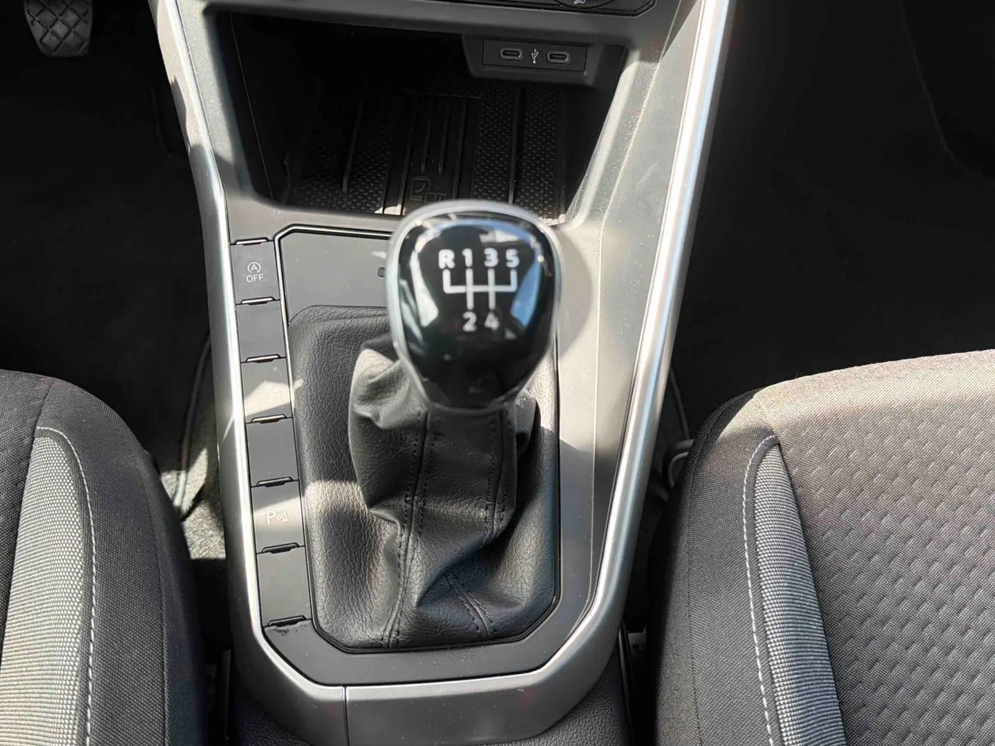Gros plan sur le levier de vitesses manuel noir de la Volkswagen Polo grise, entouré des sièges avant en tissu gris.