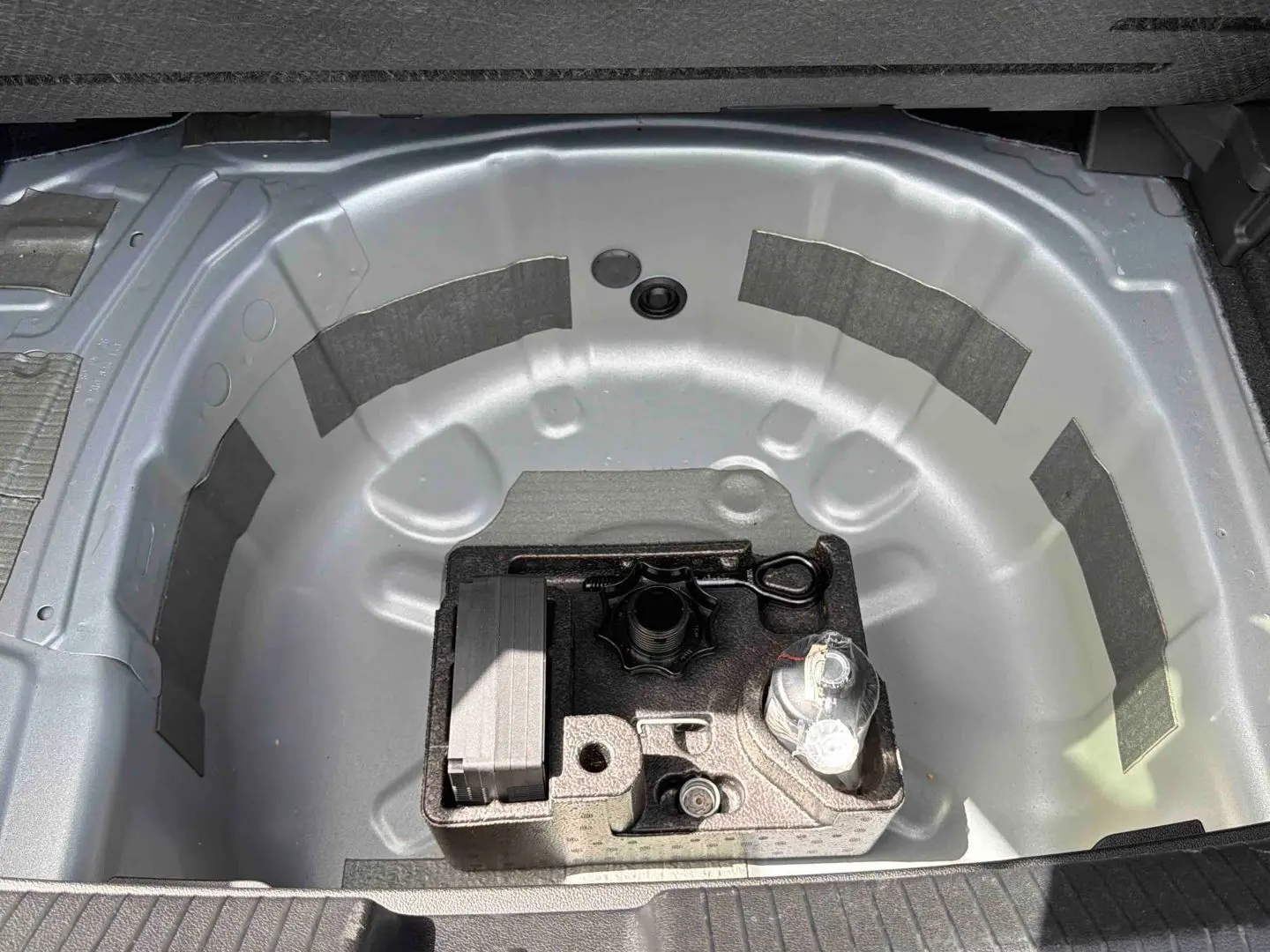Vue plongeante sur le coffre ouvert d'une Volkswagen Polo grise, montrant le rangement pour roue de secours et outils.