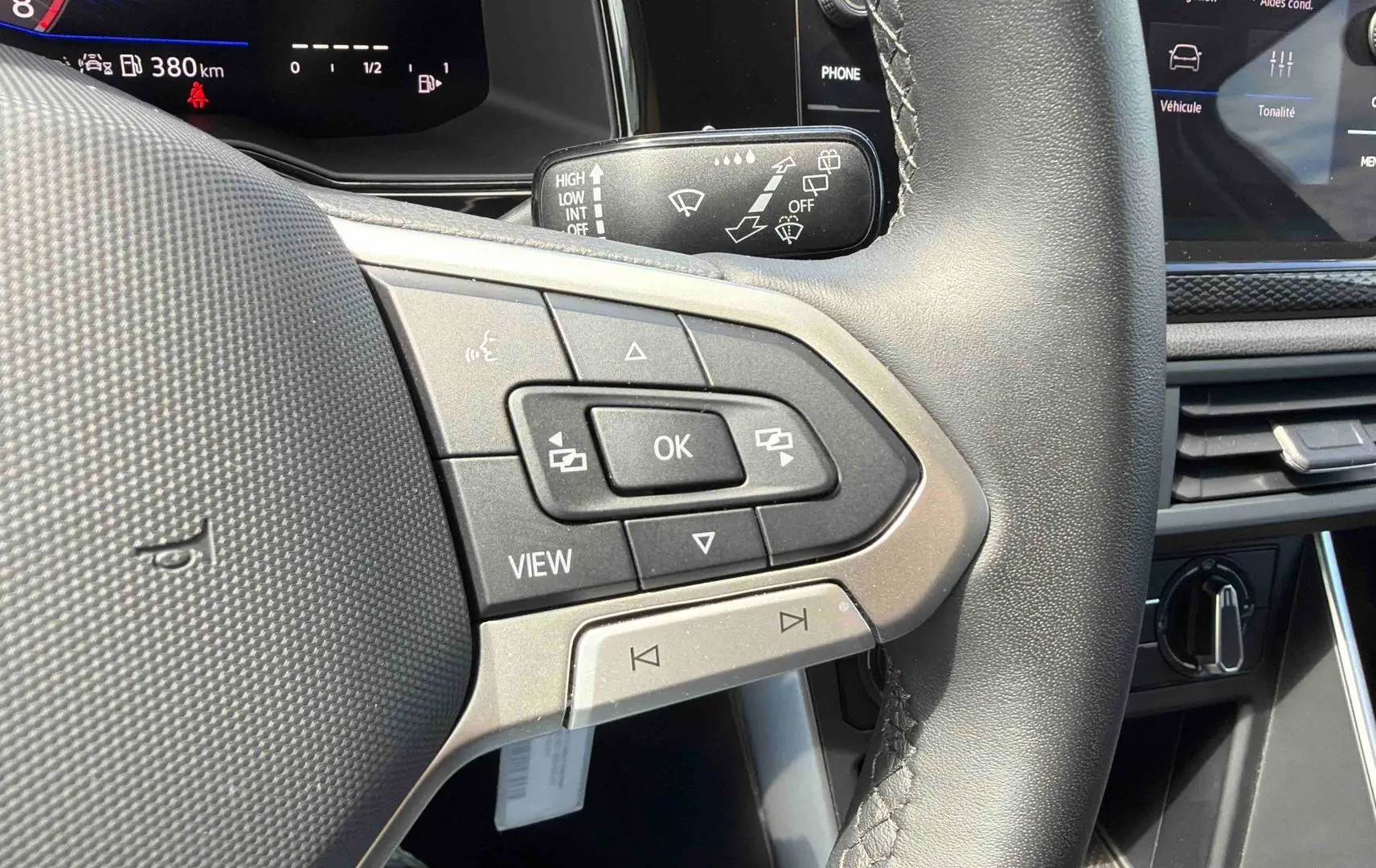 Gros plan sur les commandes au volant noir de la Volkswagen Polo 2025, avec tableau de bord digital en arrière-plan.