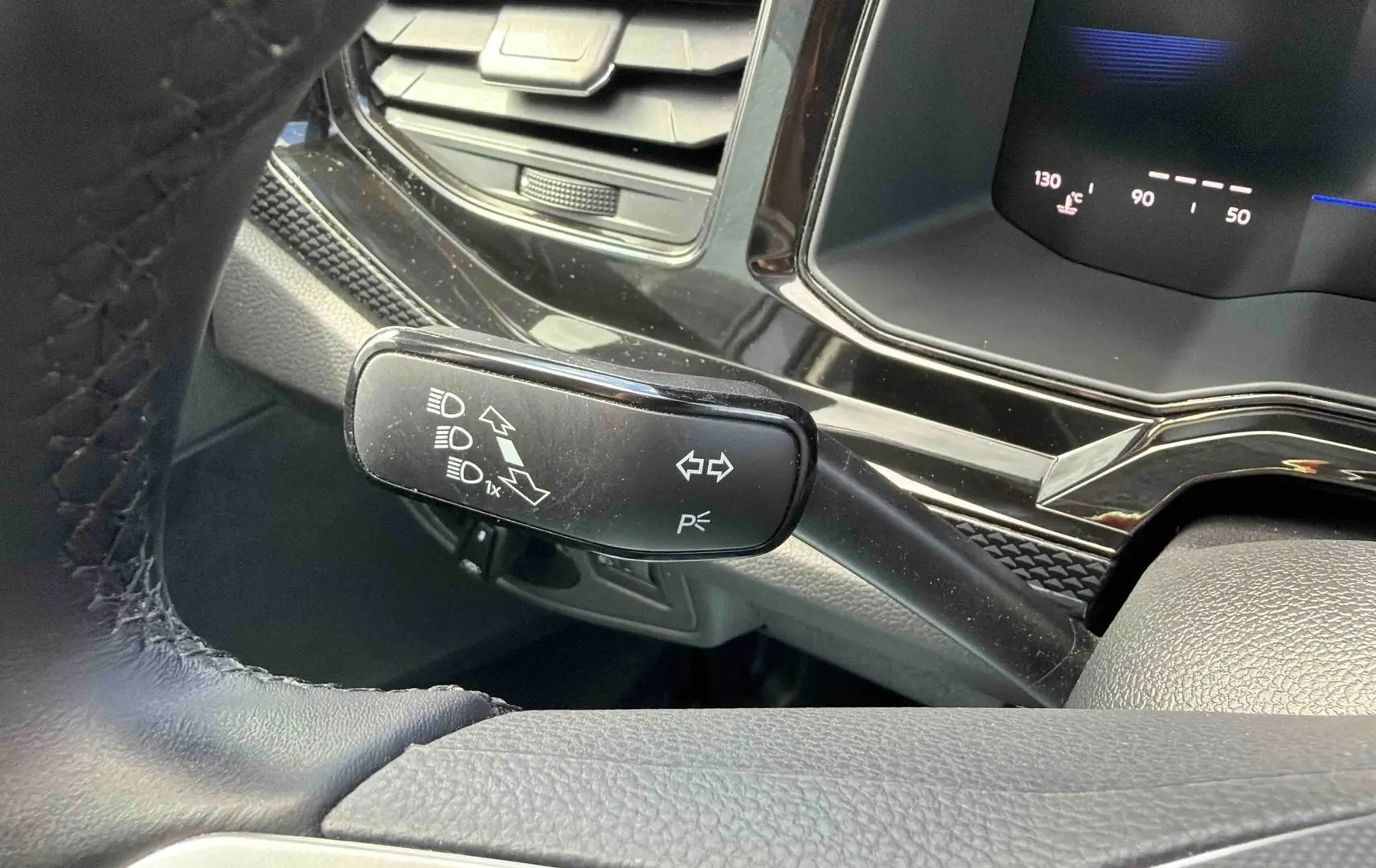 Gros plan sur la manette de clignotants noire et le tableau de bord digital d'une Volkswagen Polo grise, vue côté conducteur.