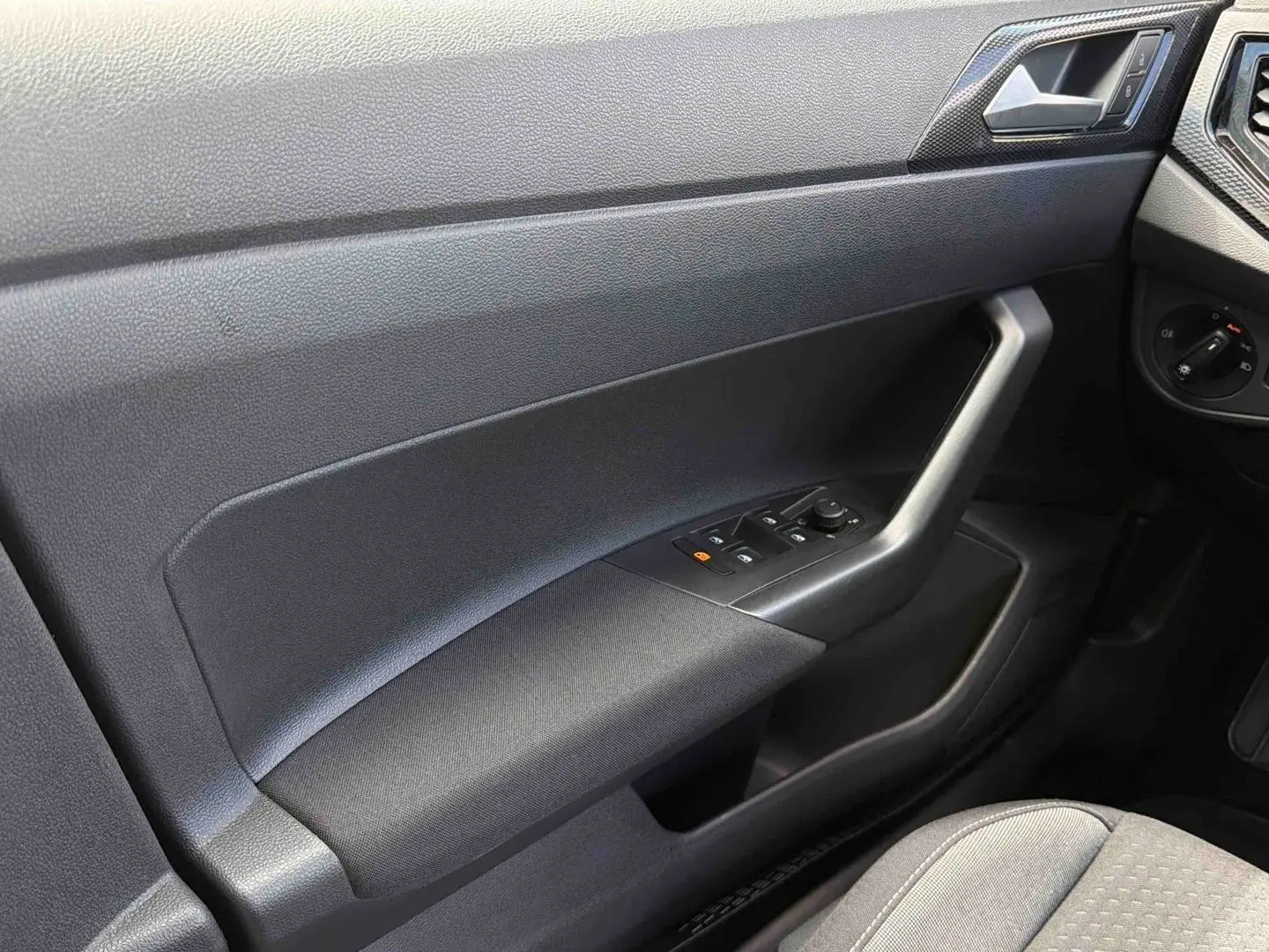 Détail de la portière côté conducteur grise avec commandes électriques des vitres et rétroviseur dans une Volkswagen Polo 2025.