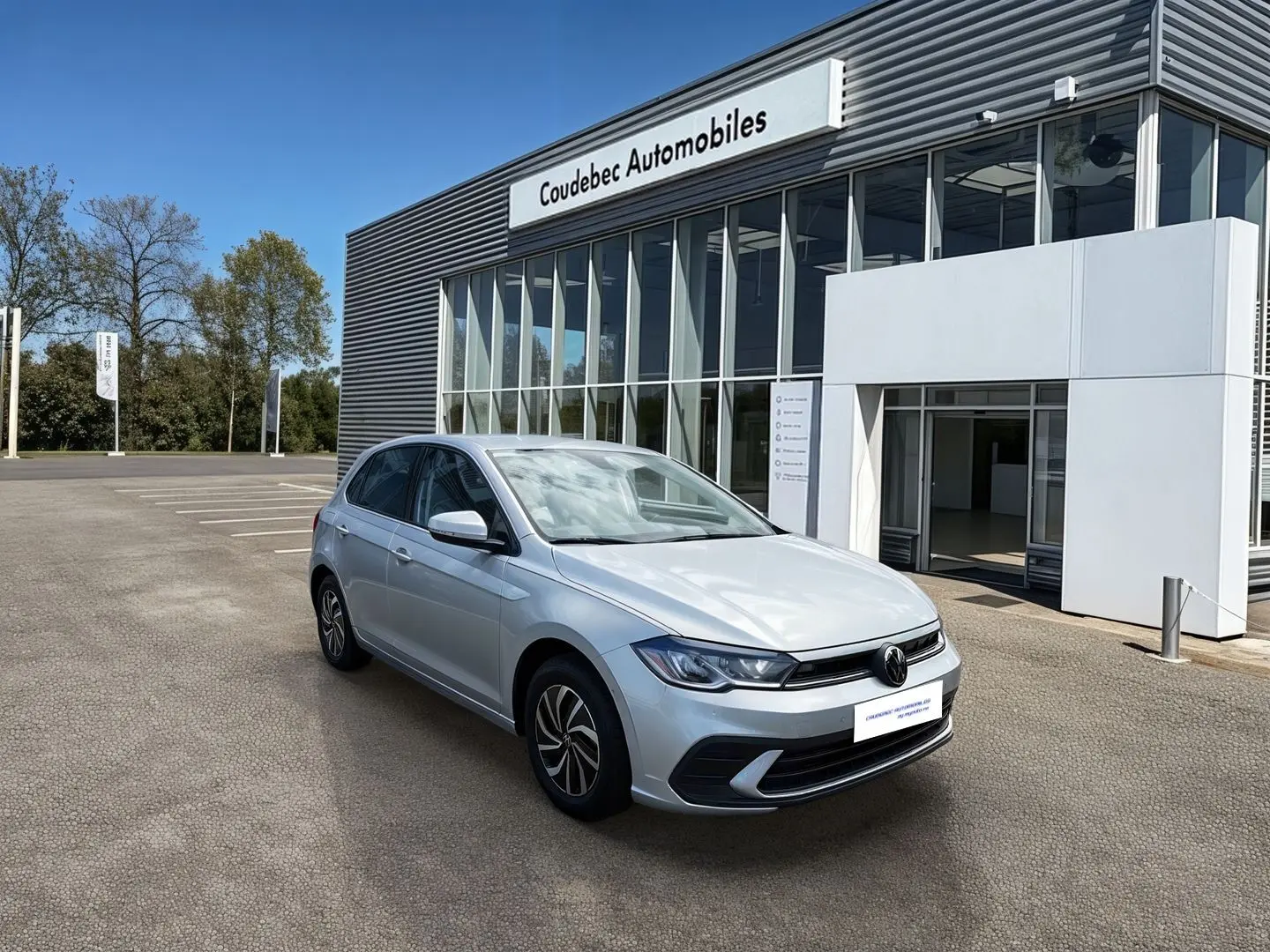 Volkswagen Polo grise vue 3/4 avant droite devant un bâtiment de concession Coudebec Automobiles.