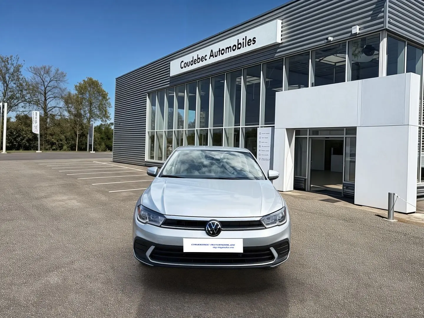 Vue avant d'une Volkswagen Polo grise 2025 stationnée devant un bâtiment commercial moderne.